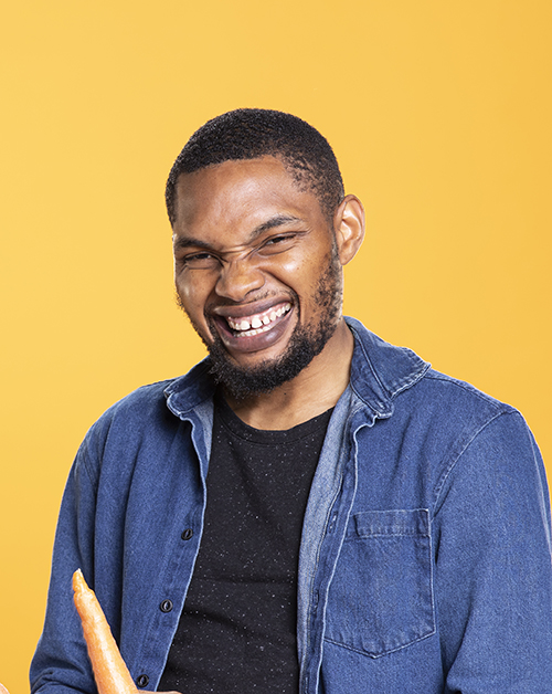 African american energetic guy pretending to play drums with carrots, advertising healthy eating and sustainable lifestyle against yellow background. Funny man acts silly with veggies.