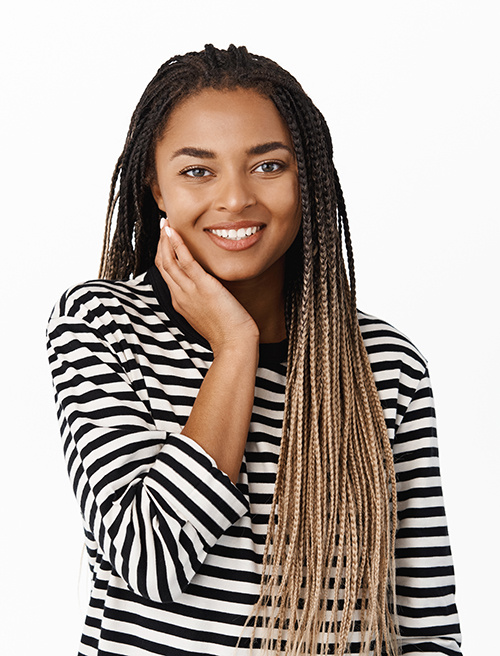 Beautiful young black girl with natural facial skin without makeup, touching her face and smiling with pleasure, standing over white background.